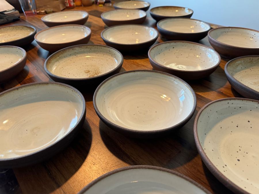 Fifteen speckled white bowls arranged on table