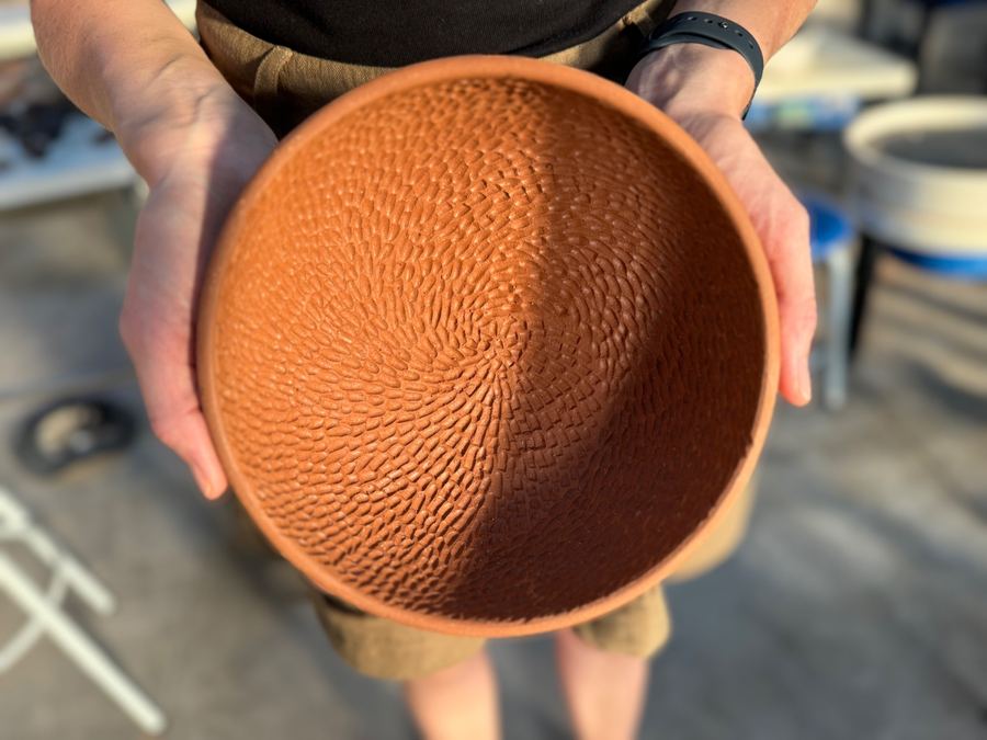 Hands holding raw terracotta bowl with woven texture